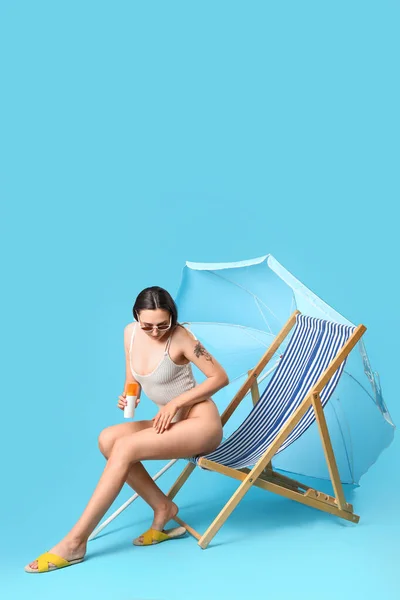 Mulher Jovem Aplicando Protetor Solar Creme Cadeira Deck Fundo Azul — Fotografia de Stock