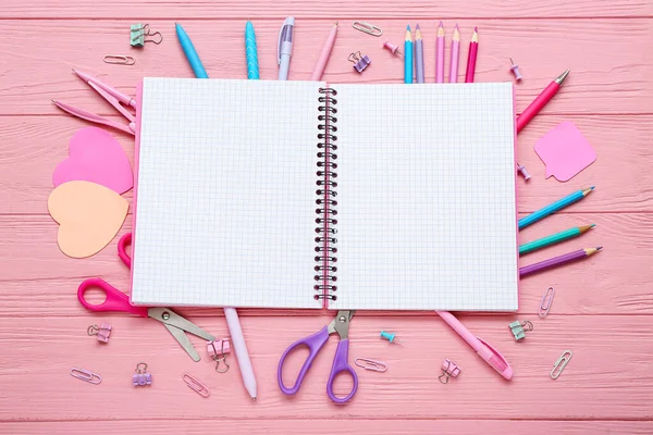 粉红木制背景的空白笔记本和不同的文具 — 图库照片