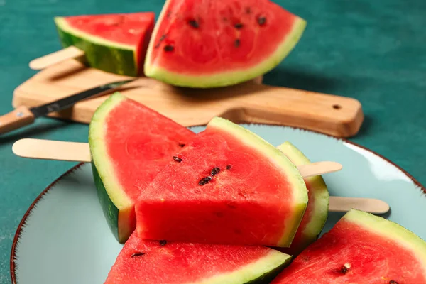 stock image Wooden board and plate with sweet watermelon sticks on green background