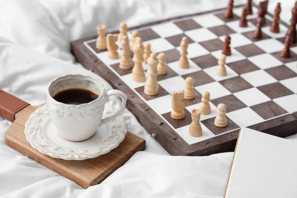 Stock image Cup of coffee with chess board on bed, closeup