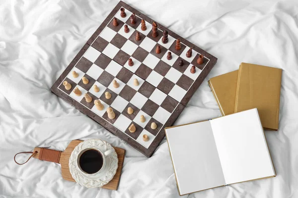 Kitaplı satranç tahtası ve yatakta bir fincan kahve.