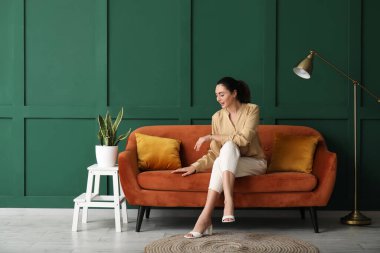 Yeşil duvarın yanındaki kırmızı koltukta oturan genç kadın.