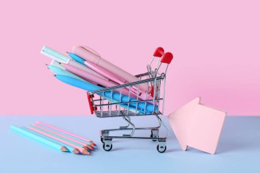 Farklı kalemleri, kalemleri ve renk arkaplanı üzerine yapışkan notları olan alışveriş arabası.