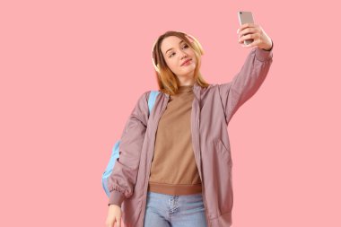 Kulaklıklı kız öğrenci pembe arka planda selfie çekiyor.