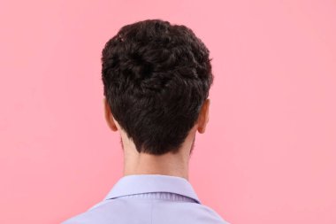 Pembe arka planda, şık saç stili olan esmer genç adam.