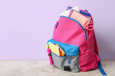 Lacivert duvarın yanındaki açık grunge masasında defter, işaret ve makas içeren renkli okul çantası