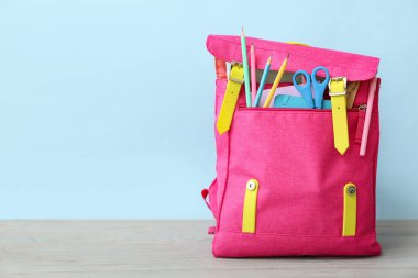 Mavi duvarın yanında, üzerinde makas, defter ve kalemler olan pembe okul çantası.