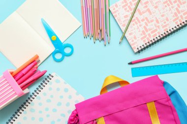 Okul çantasından yapılmış çerçeve ve mavi arkaplanda farklı kırtasiye malzemesi, yakın plan