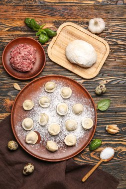 Ahşap arka planda pişmemiş hamur köfteleri ve malzemelerle dolu bir tabak.