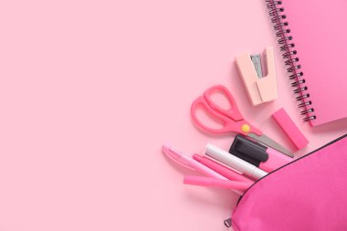 Pembe zemin üzerinde farklı kırtasiye malzemesi olan defter ve kalem kutusu.