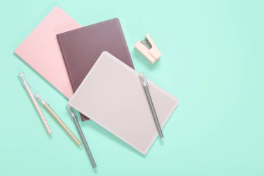 Kalemleri ve turkuaz arka planda zımbası olan farklı renkli defterler