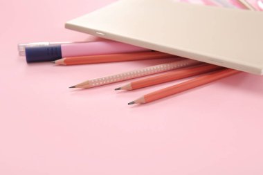 Pembe arkaplanda farklı kırtasiye malzemesi olan defter