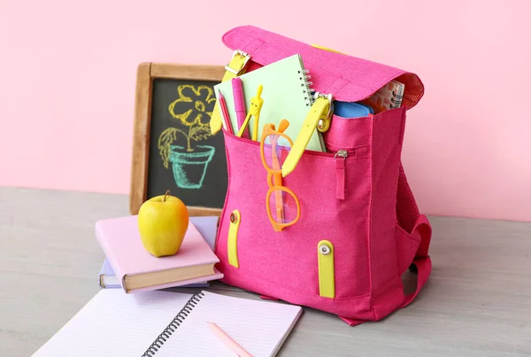 粉红校服背包 粉笔画花和苹果放在靠近彩墙的灰色木制桌子上 — 图库照片