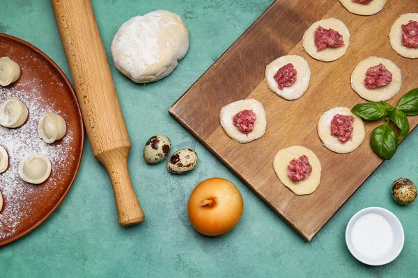 stock image Wooden board of raw dough with minced meat and ingredients for preparing dumplings on grunge background