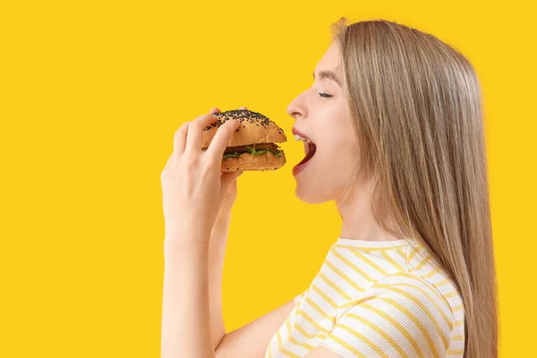 Jovem Mulher Comendo Hambúrguer Saboroso Fundo Amarelo Close — Fotografia de Stock