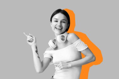 Kulaklıklı mutlu genç kadın gri arka planda bir şey gösteriyor.