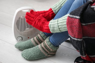 Evdeki elektrikli fan ısıtıcısının yanında elleri ısıtan kadın, yakın çekim.