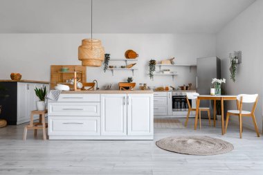 Şık buzdolabı, tezgah, raf, masa ve sandalyeli aydınlık mutfağın içi.