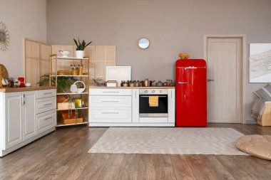 Mutfağın içinde kırmızı buzdolabı, tezgah ve raf ünitesi var.