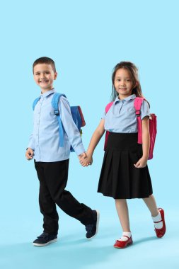 Açık mavi arka planda el ele tutuşan küçük okul çocukları