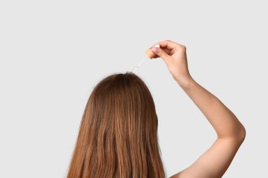 Genç bir kadın arka planda, arka planda saç bakımında kozmetik yağ kullanıyor.