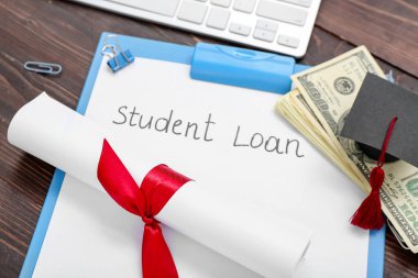 Diploma, dolar banknotları, mezuniyet şapkası ve ahşap arka planda STUDENT kredisi olan kağıt kağıtlar.