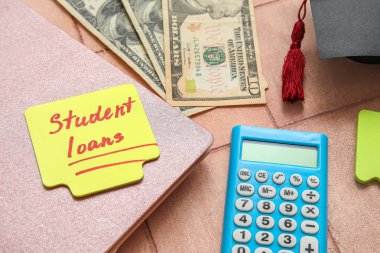 Metin Öğrenci kredileri, dolar banknotları, hesap makinesi, not defteri ve arkaplanda mezuniyet şapkası olan yapışkan bir not.