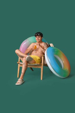 Sandalyede yaz kokteyli içen ve yeşil arka planda yüzen genç adam.