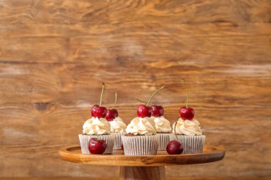 Tahta arka planda vişneli keklerin yanında dur.