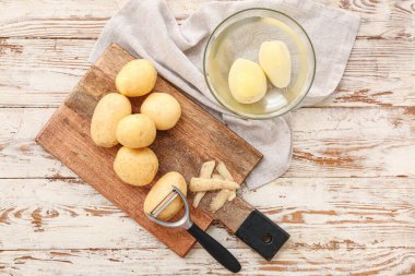 Beyaz ahşap arka planda çiğ patatesli yemek ve kase.