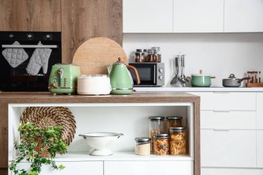 Tost makinesi, elektrikli su ısıtıcı, meyve sıkacağı ve modern mutfakta ahşap masa üzerindeki tahta kesme tahtası.