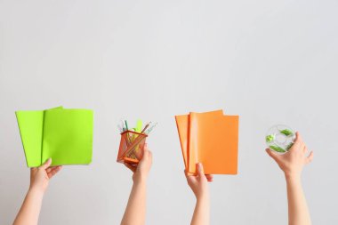 Gri arka planda okul malzemelerini tutan kadın eller.