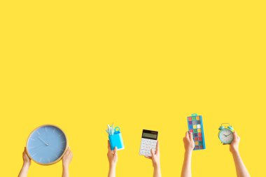 Birçok el sarı arka planda okul malzemelerini tutuyor.