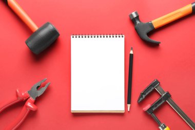 Kırmızı arka planda farklı araçlar ve defter içeren kompozisyon. İşçi Bayramı kutlamaları