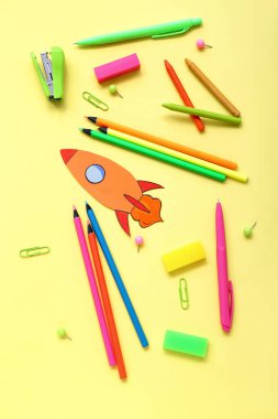 Paper rocket with school stationery on yellow background