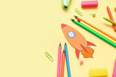 Paper rocket with school stationery on yellow background