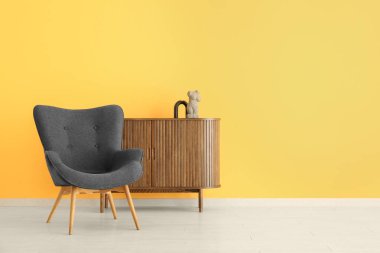 Sarı duvarın yanında heykeli olan şık siyah koltuk ve dolap.