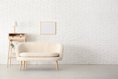 Rahat beyaz kanepe ve tuğla duvara yakın çerçeveli raf ünitesi.