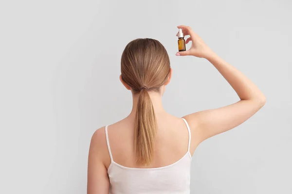 Stock image Young woman with cosmetic oil for hair treatment on light background, back view