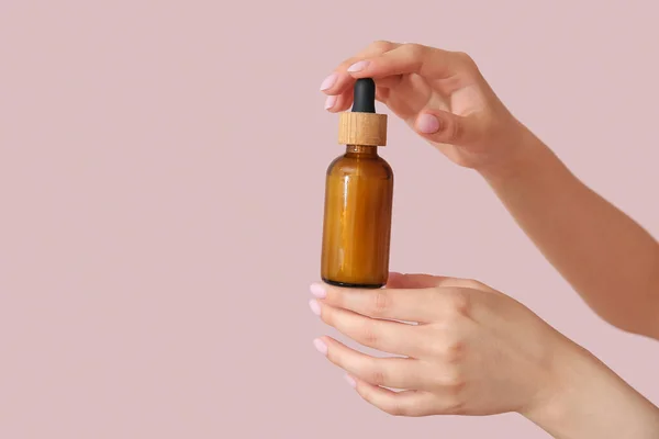 ピンクの背景に化粧品油のボトルと女性の手 — ストック写真