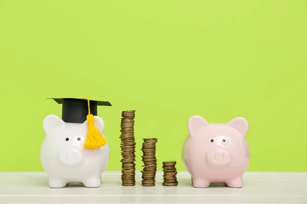 有一堆堆硬币和绿色背景的白桌子上的毕业帽的小猪银行 学生贷款概念 — 图库照片