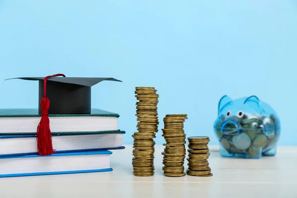 青い背景に白いテーブルの上のコイン 卒業キャップと貯金箱のスタック 学生ローンの概念 — ストック写真