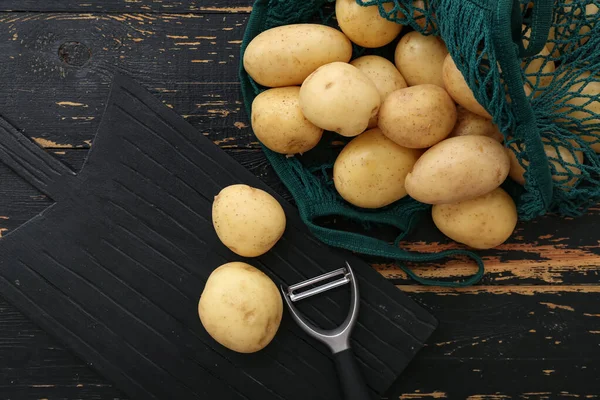 Brett Und Saitentasche Mit Rohen Kartoffeln Auf Schwarzem Holzhintergrund — Stockfoto
