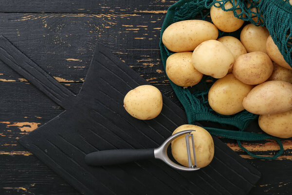 Доска и веревочная сумка с сырым картофелем на черном фоне