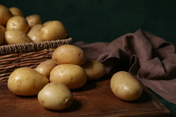 Holzbrett Und Weidenschachtel Mit Rohen Kartoffeln Auf Grünem Hintergrund Nahaufnahme — Stockfoto