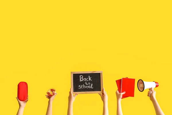 多くの手は 黄色の背景に戻って学校にテキストと学校用品や黒板を保持 — ストック写真