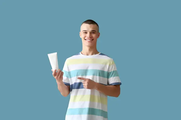 幸せな若い男指すでボトルの日焼け止めクリーム上の青の背景 — ストック写真