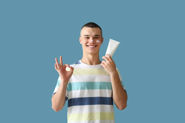 Szczęśliwy Młody Człowiek Butelką Kremu Opalania Pokazując Gest Niebieskim Tle — Zdjęcie stockowe