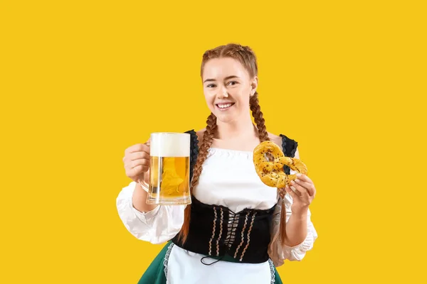 若いです女性で伝統的なドイツの服にビールとプレッツェルで黄色の背景 — ストック写真
