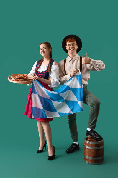 Молодая пара в традиционной немецкой одежде с пивом, закусками и баварским флагом на зеленом фоне